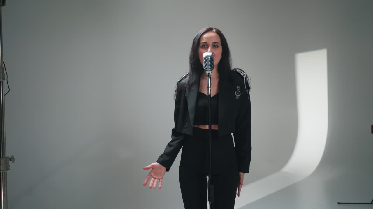 cantante femenina emotiva en traje negro actuando enérgicamente en un micrófono con un tecladista masculino en el fondo en un conjunto minimalista