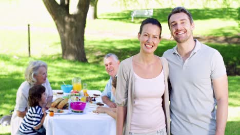 Mutter-Und-Vater-Lächeln-In-Die-Kamera,-Während-Die-Familie-Hinter-Ihnen-Zu-Mittag-Isst