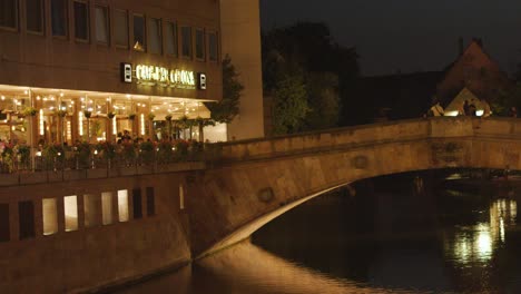 illuminated riverside restaurants and historic stone bridge at night, gentle camera pan, warm lighting