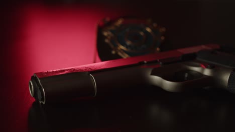 Wide-view-of-gun-and-police-badge-on-a-dark-surface-with-flashing-red-and-blue-light-in-the-background