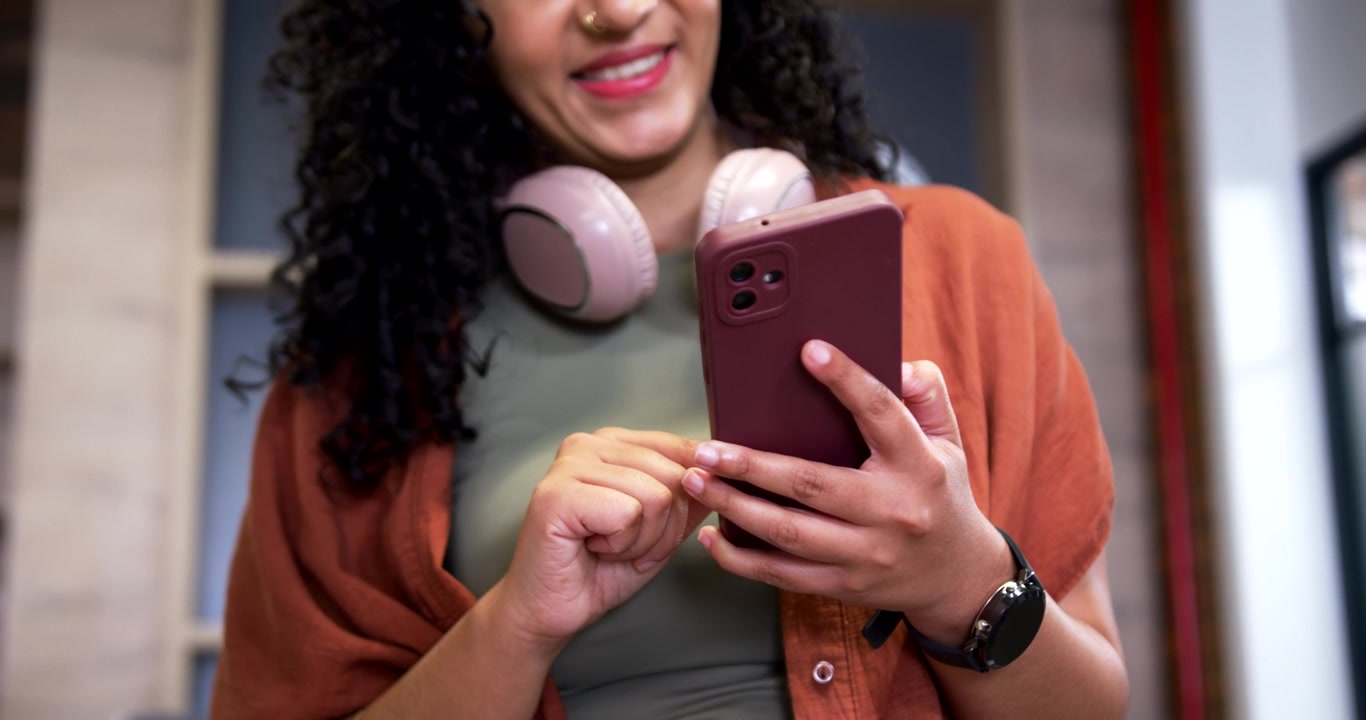 African American woman receiving alert, tapping phone and smiling at office replying to messages