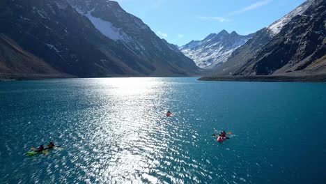 Luftbildwagen-In-Drei-Kajaks-In-Der-Laguna-Del-Inca-Mit-Der-Sonne,-Die-Sich-Auf-Dem-Kristallblauen-Wasser,-Schneebedeckten-Bergen-Im-Hintergrund-Widerspiegelt