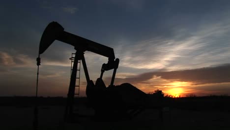 medium shot of a silhouetted oil pump turning in the new mexico desert pumping petroleum