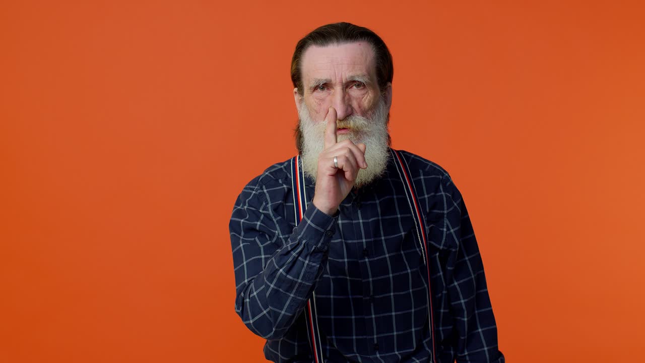 Elderly bearded man presses index finger to lips makes silence gesture sign do not tells secret
