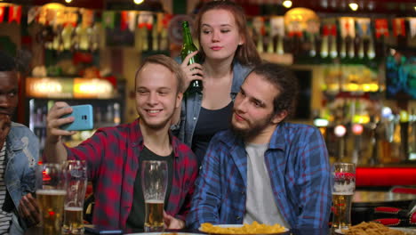 un grupo de amigos multiétnicos descansando en el bar. amigos toman una foto en el teléfono en el bar hacen una foto compartida en el teléfono. fiesta con amigos en el bar con cerveza.