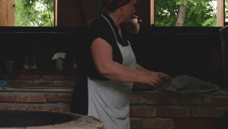 woman in apron pours out ashes on traditional tone oven