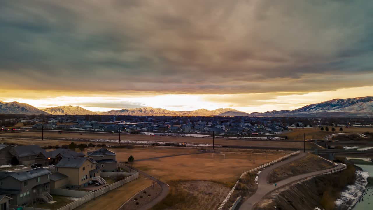 Gloomy cloudscape above the sunshine with an urban area below and the snow mountains in the distance - aerial hyperlapse