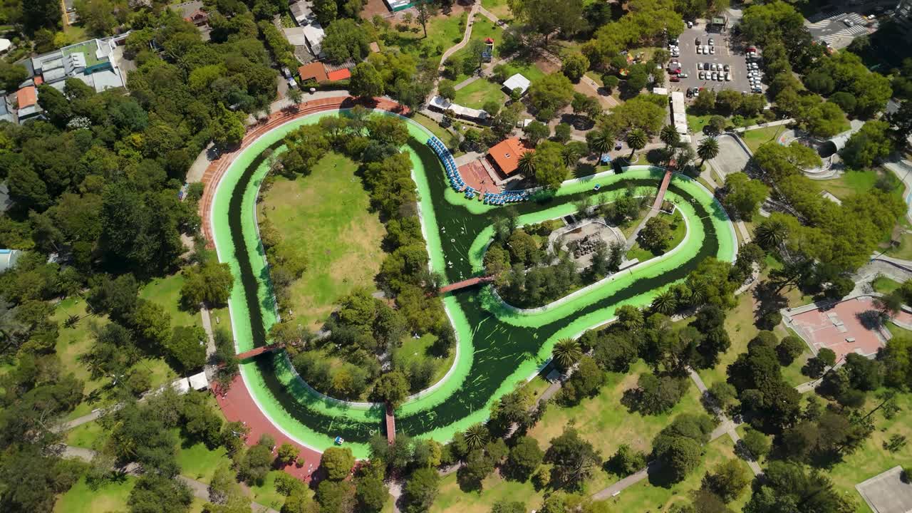 Parallax aéreo sobre la laguna del Parque La Carolina, un serpenteante canal de agua verde con muelle para botes de remo y dosel arbóreo en Quito