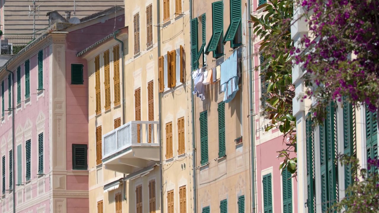 Inquadratura fissa di vivaci facciate mediterranee con bucato steso e fiori viola in pieno sole.