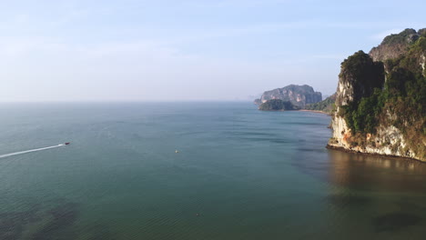 Boat-cruising-in-vast-coastal-sea-waters-below-steep-limestone-cliffs