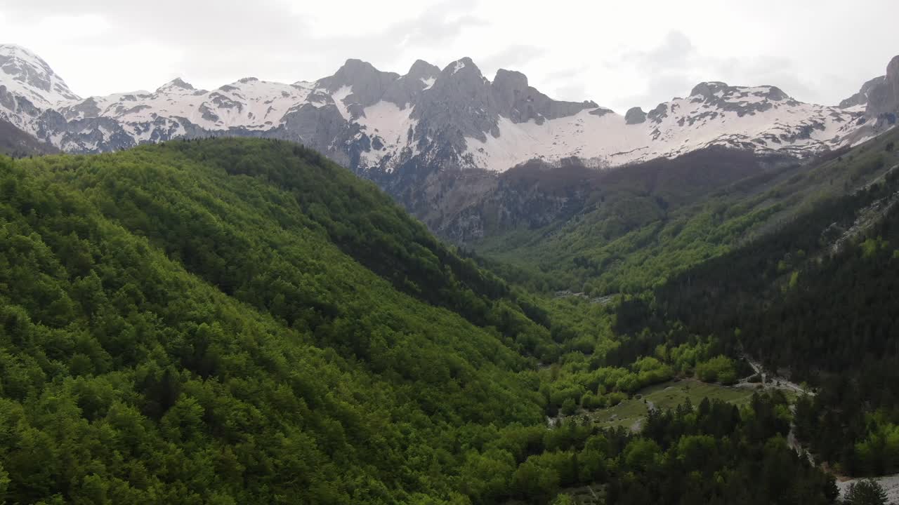 vista de avión no tripulado en albania volando en los alpes mostrando bosque verde en un valle rodeado de montañas con picos nevados en valbon?