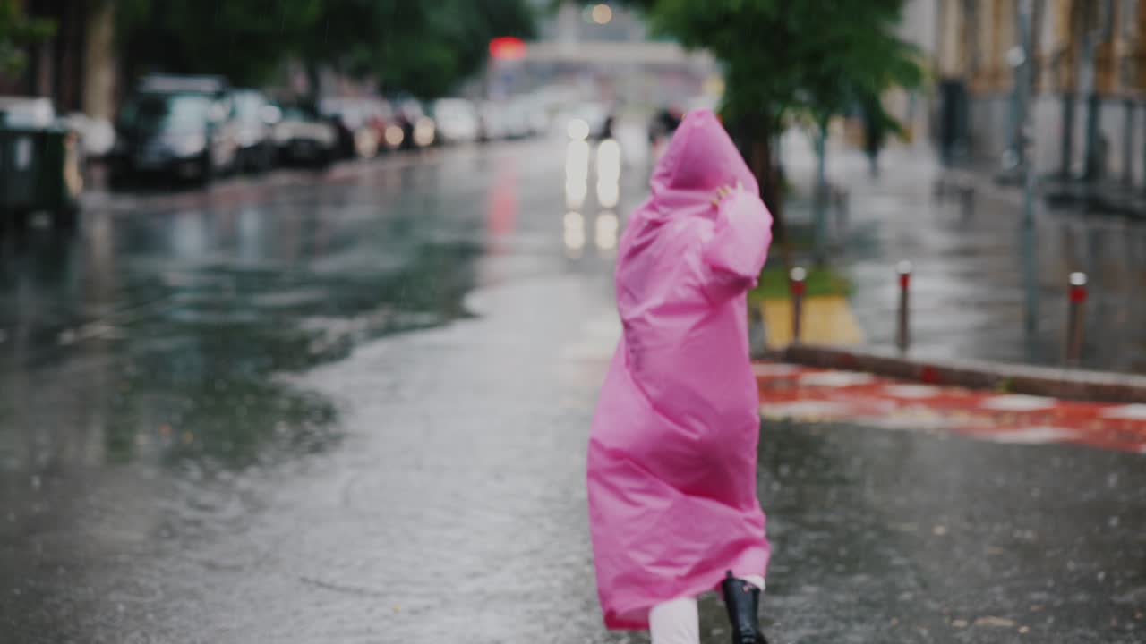 핑크색 레인코트 를 입은 여자 가 비 를 고 있다
