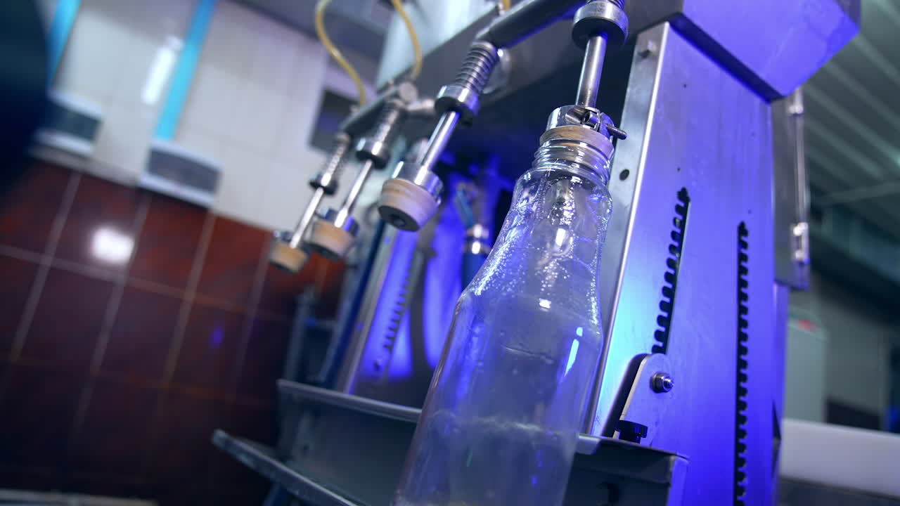 Glass bottles being put under the automatic system of filling. Freshly made apple juice poured into the bottles at modern food factory.
