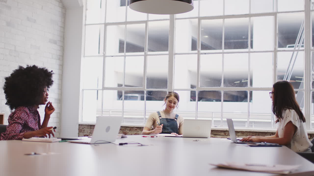 Three millennial creative women in discussion at a table in a meeting room