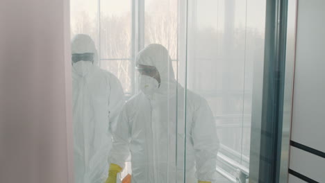 two cleaning men wearing personal protective equipment getting out of glass elevator inside an office building