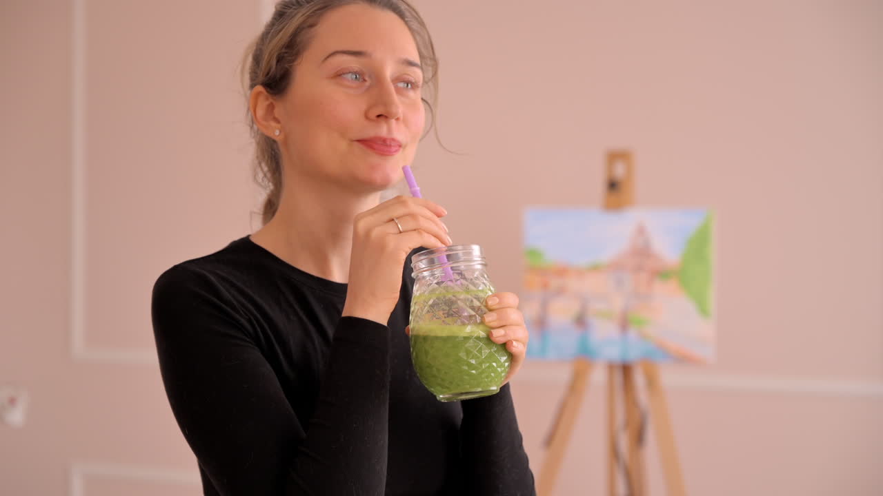 Woman in a black shirt drinking green juice from a glass
