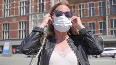 dutch woman with sunglasses put on mask in front of amsterdam central station during corona virus pandemic