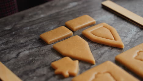 close up woman carefully removes excess dough from freshly cut shapes on baking surface, preparing cookies with intricate designs for baking in cozy kitchen setting