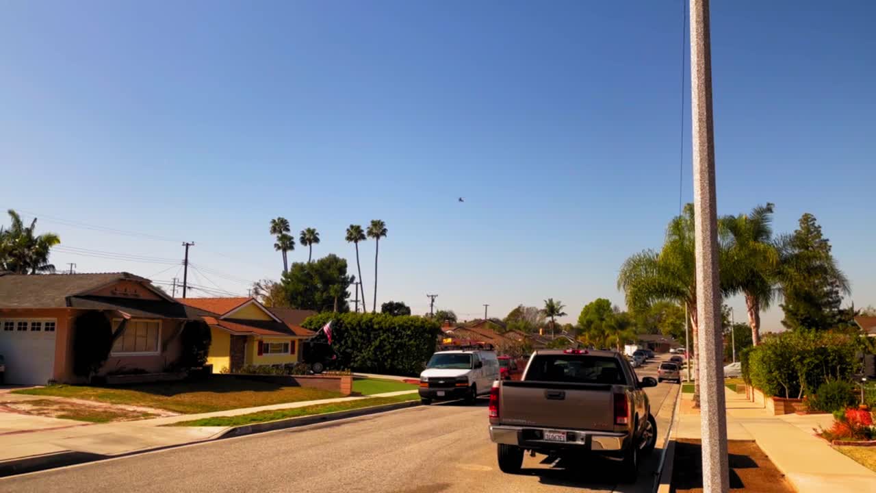 Helicopter flying from far away towards the camera over some houses in a southern California neighborhood.