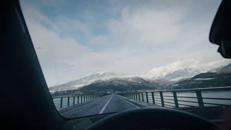 tranquil mountain scenery from inside of a car driving on lake bridge