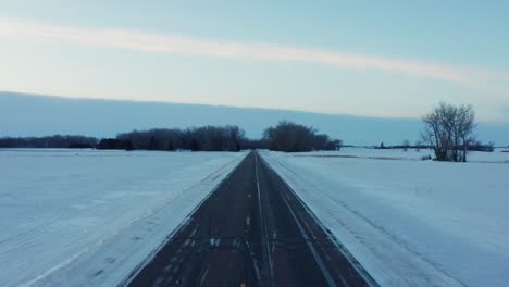 Cinematic-aerial-shot,-flying-down-the-middle-of-an-icy-country-road-in-rural-Minnesota