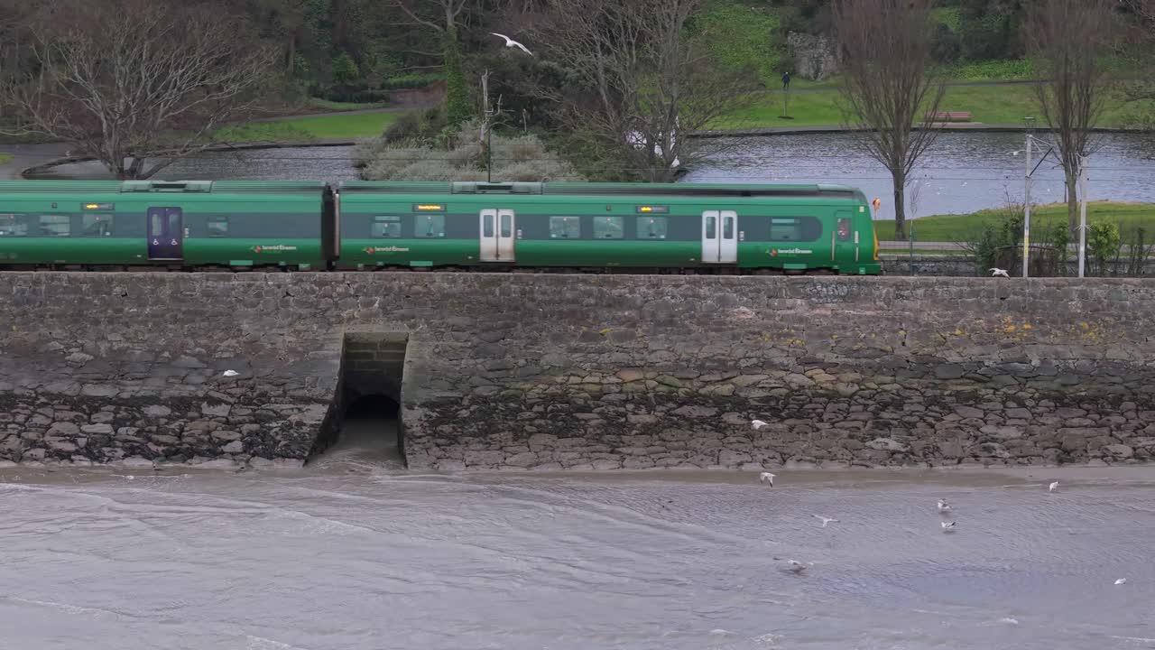 Traveling Train Over Railways Along The River At Blackrock District In Dublin, Ireland. Wide Shot