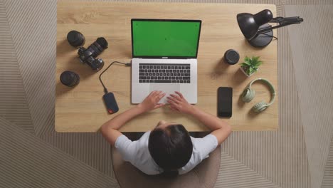 top view of asian woman video editor thinking about something then raising index finger while using green screen laptop and smartphone next to the camera in the workspace at home