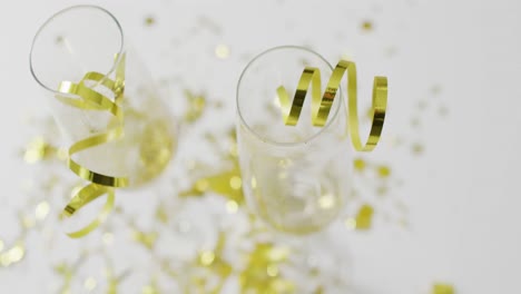 overhead video of champagne glasses with gold streamers and confetti on white, with copy space