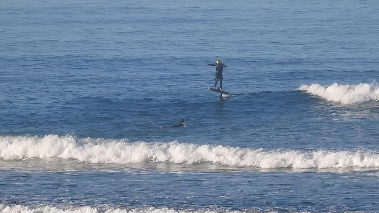 Foiling on ocean wave aerial view from behind on clear summer's day,