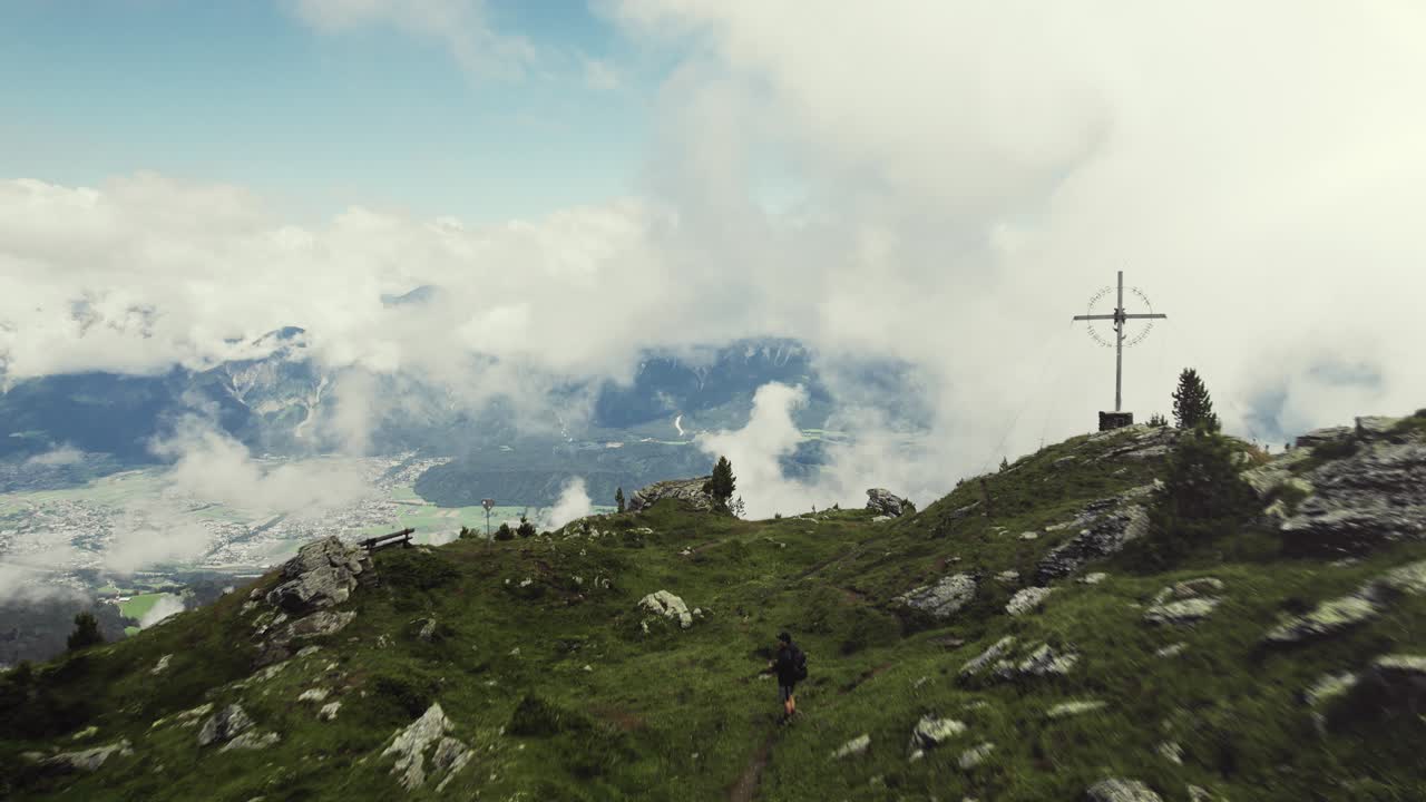 Aerial drone shot of a grass covered mountain top with a person hiking along a small trail