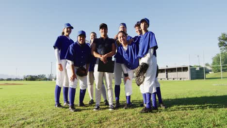 group portrait of diverse team of female baseball players and coach standing on sunny pitch smiling