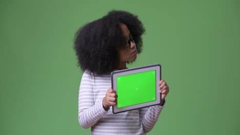 young cute african girl with afro hair thinking while showing digital tablet to camera