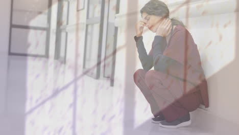 Animation-of-rain-on-window-over-unhappy-caucasian-female-doctor-crouching-in-hospital-corridor