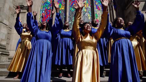 a video still of a choir in blue and gold robes singing on cathedral steps