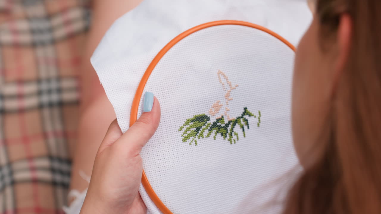 Close up rear view of student holding embroidery hoop stitching delicate tree design on white fabric, soft natural daylight reflecting on hands, peaceful creative moment