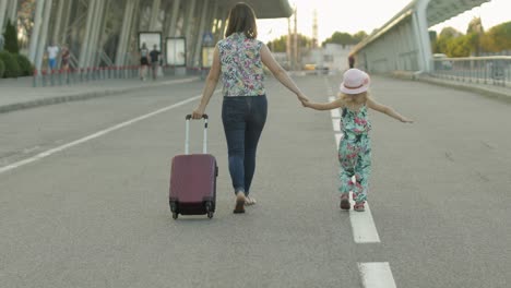 Mother-and-daughter-walking-outdoors-to-airport.-Woman-carrying-suitcase-bag.-Child-and-mom-vacation