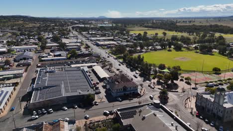 drone footage glides above city streets, parked cars, and a green park under clear daylight, capturing urban mobility and town layout from a high angle