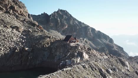 Inclinación-Hacia-Abajo:-Vista-Por-Drones-De-Una-Cabaña-De-Madera-En-Los-Alpes-Suizos,-En-Montañas-Rocosas