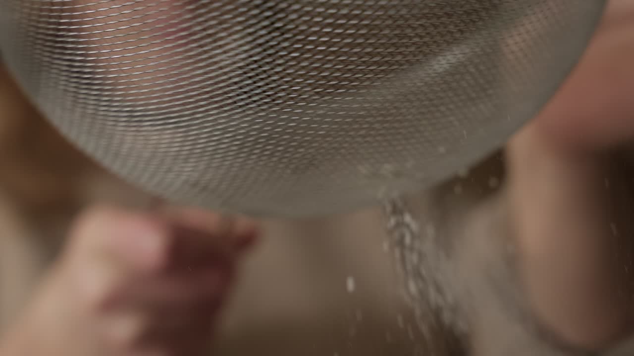 Slow motion close up of fine powder falling through kitchen sieve