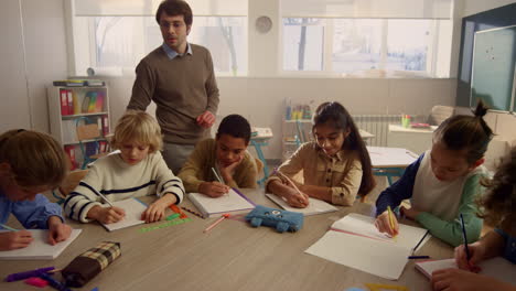 Schüler-Zeichnen-Am-Runden-Tisch-In-Notizbüchern.-Fröhliche-Kinder,-Die-Bleistifte-Verwenden