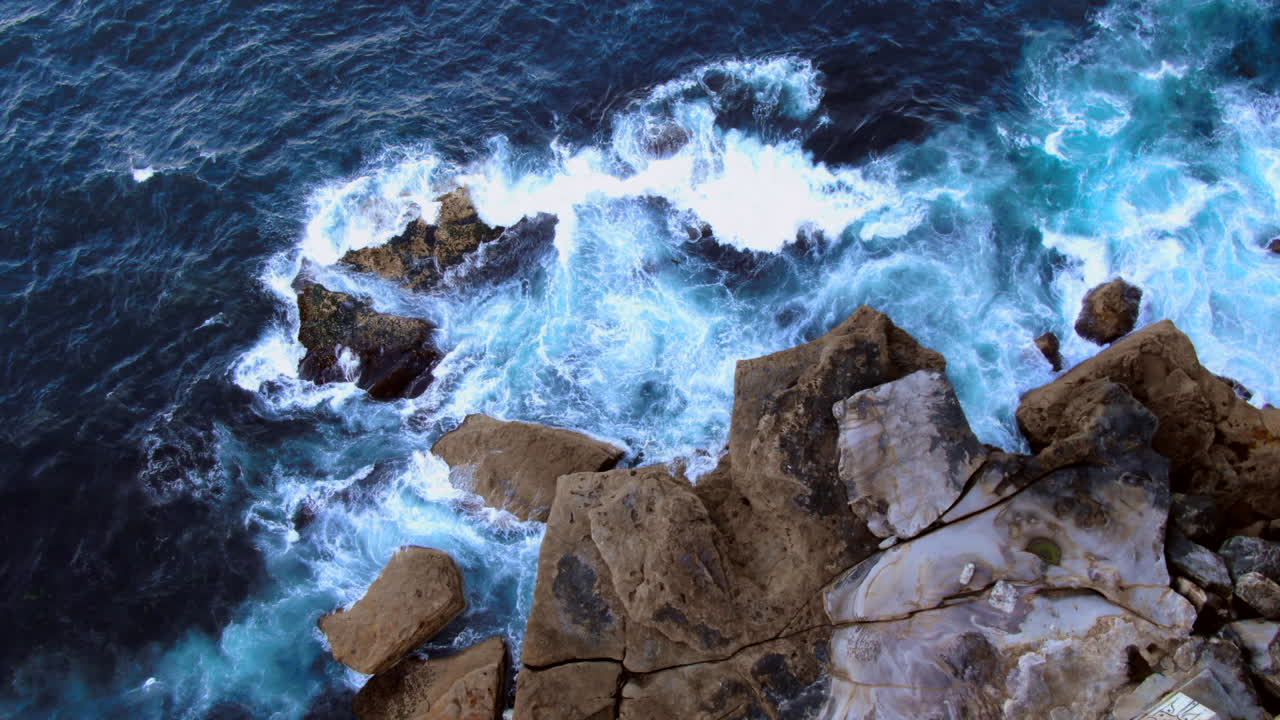 aérea: zoom sobre las olas del océano rompiendo sobre las rocas en north bondi, sydney, australia