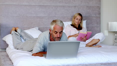 man lying on his bed with a laptop next to his wife