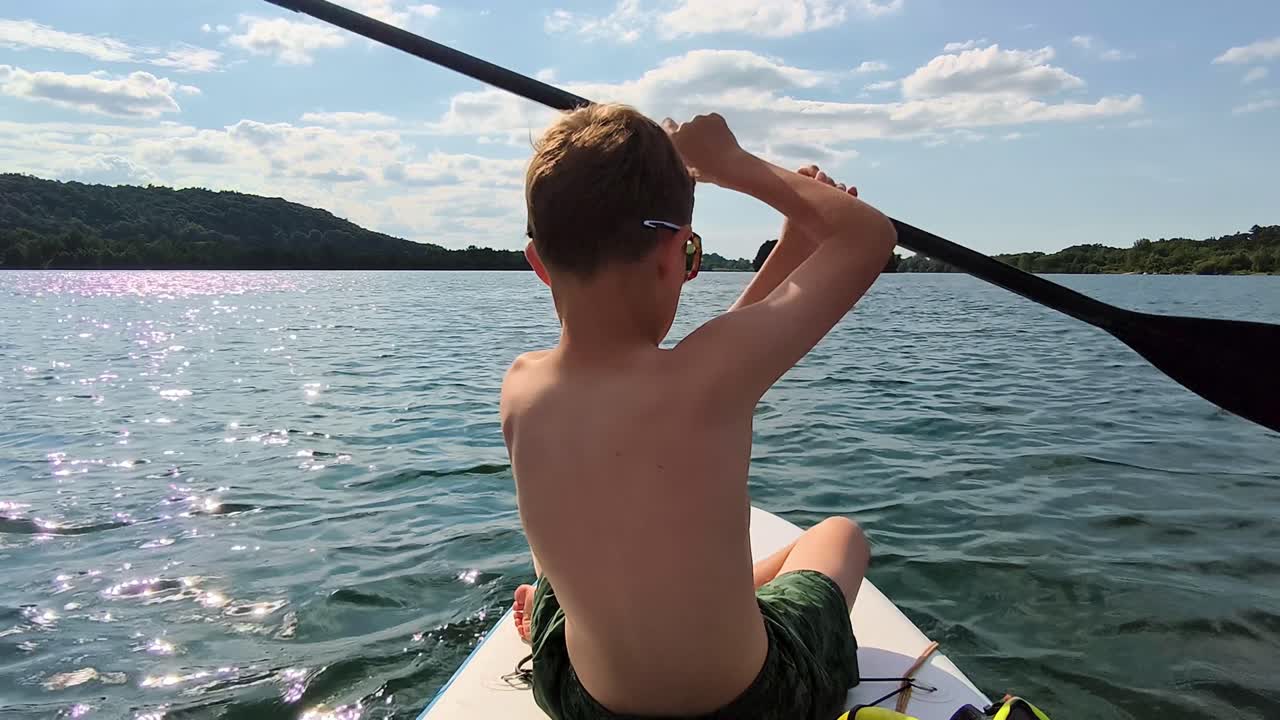 Child on a paddleboard gliding across a tranquil lake, enjoying peaceful nature, rearview