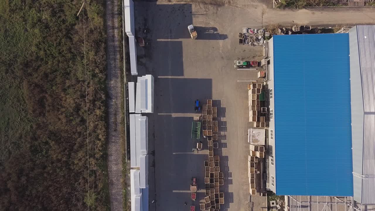 trucks are transporting apples on trailers in the territory of warehouse with wooden boxes near an apple orchard in the field. Aerial view