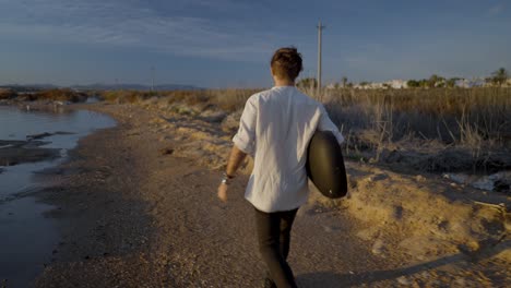 man walking with guitar on a scenic beach path