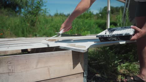 Zugeschnittenes-Bild-Eines-Mannes,-Der-Im-Freien-Holzbretter-Mit-Weißer-Farbe-Mit-Einem-Rollpinsel-Bemalt