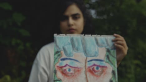 Slow-motion-shot-of-Young-Asian-woman-holding-a-painting-in-front-of-camera-with-a-dark-background