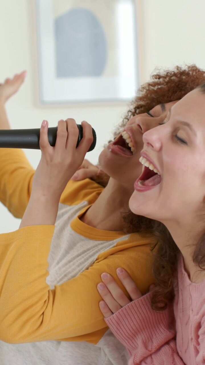 Video verticale: Cantante solista in senape che tiene un microfono, esorta il partner in rosa a unirsi a casa.