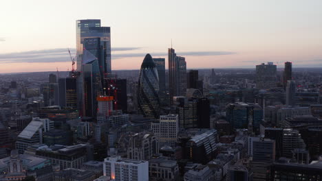 Fly-around-modern-city-district-with-tall-skyscrapers-in-evening.-Colourful-sky-after-sunset.-London,-UK