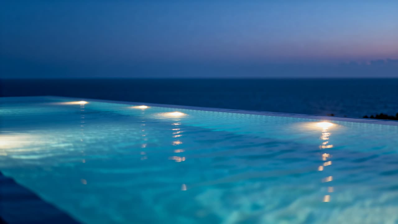 Rippling illuminated infinity-edge pool water reacting to light breeze at dusk, with three lights